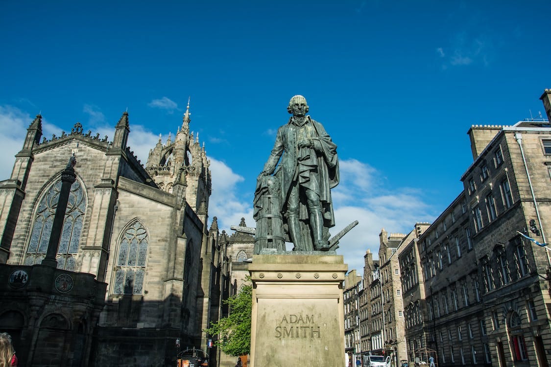 Free Man in Coat Statue Near Buildings Stock Photo