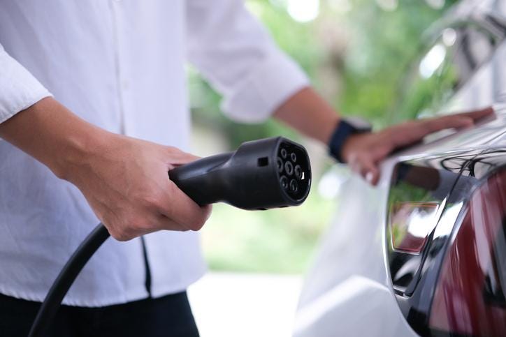 A person holding a power supply plugged into a car

Description automatically generated