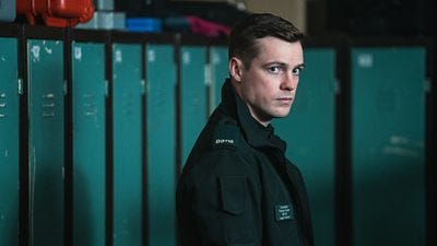 A man in police uniform stands in a locker room looking wary of something off screen