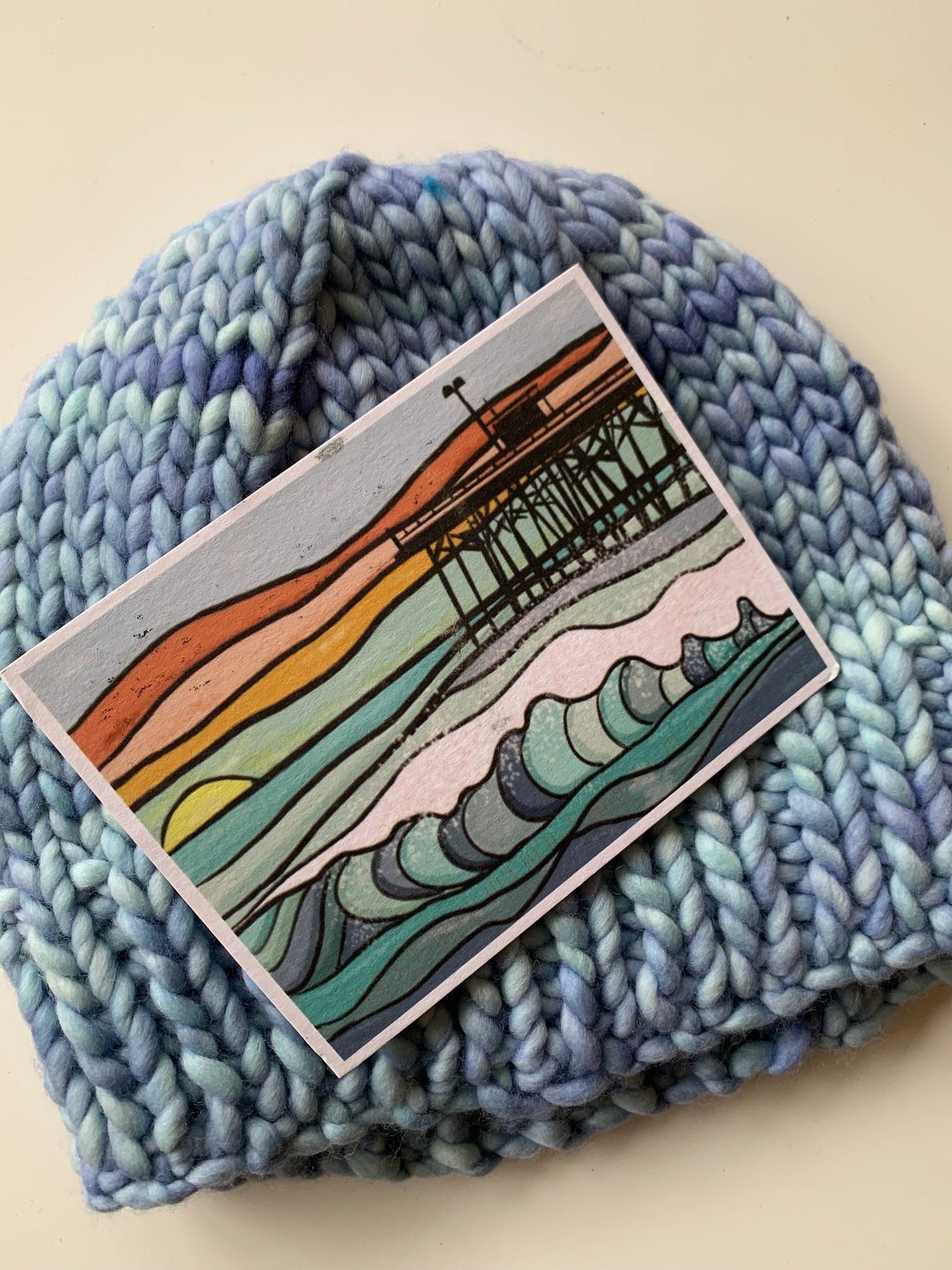 watercolor postcard of a pier on top of a blue variated knit hat