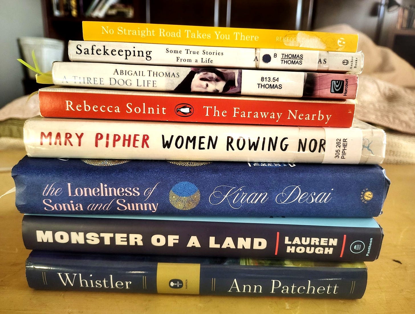 stack of 8 books in various colors with the spines showing their titles: safekeeping by abigail thomas a three dog life by abigail thomas, whistler by ann patchett, women rowing north by mary pipher, the faraway nearby by rebecca solnit, the loneliness of sonia and sunny by kiran desai, monster of a land by lauren hough and others