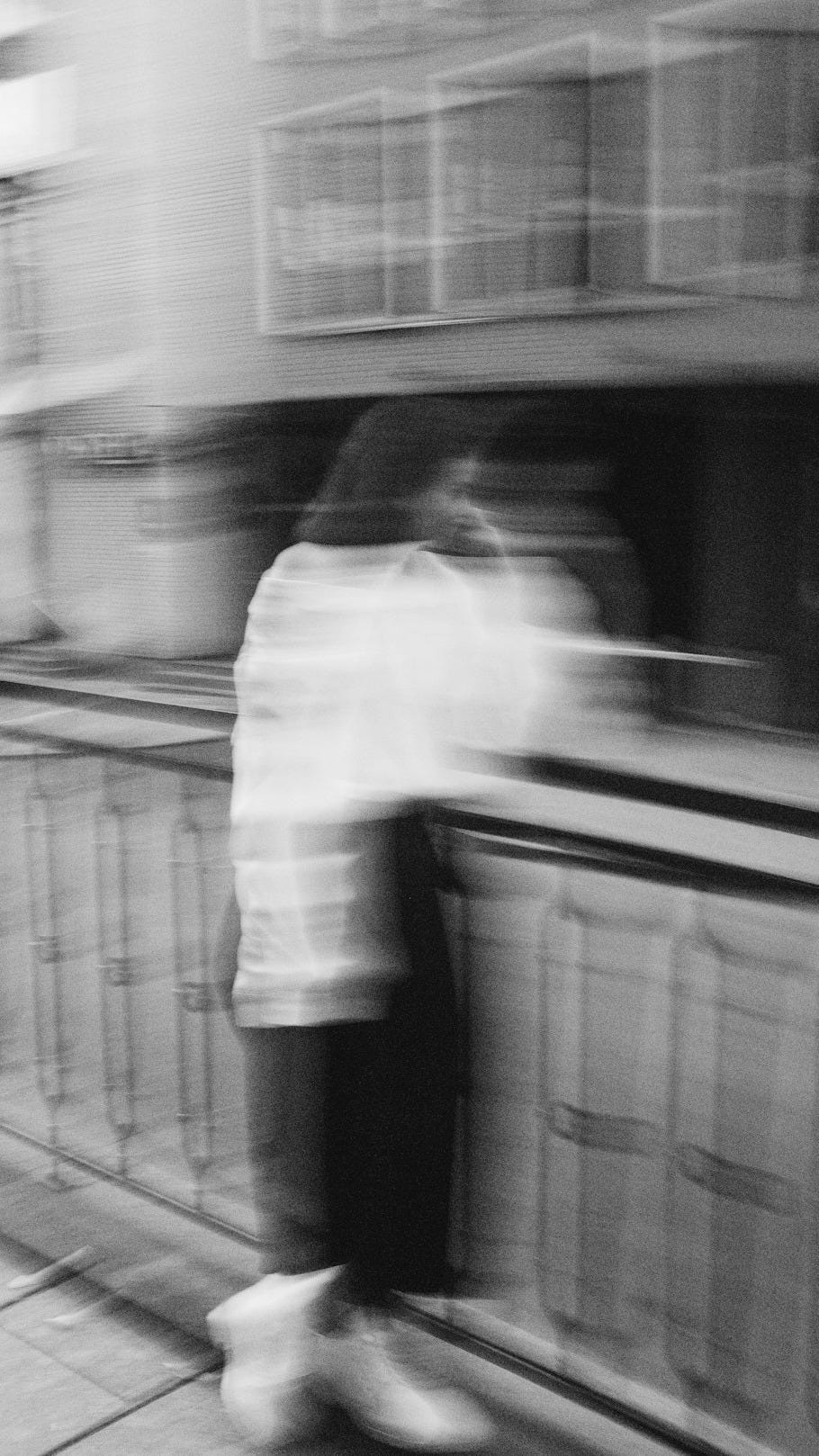 grayscale photo of man in white dress shirt and black pants standing on train station