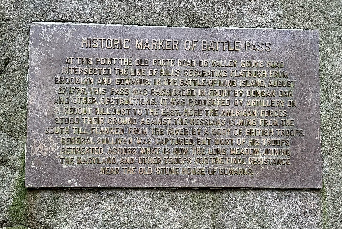 A close up of the Battle Pass plaque. It reads: HISTORIC MARKER OF BATTLE PASS / AT THIS POINT THE OLD PORTE ROAD OR VALLEY GROVE ROAD / INTERSECTED THE LINE OF HILLS SEPARATING FLATBUSH FROM / BROOKLYN AND GOWANUS. IN THE BATTLE OF LONG ISLAND, AUGUST 27, 1776, THIS PASS WAS BARRICADED IN FRONT BY DONGAN OAK / AND OTHER OBSTRUCTIONS. IT WAS PROTECTED BY ARTILLERY ON / REDOUT HILL JUST TO THE EAST. HERE THE AMERICAN FORCES / STOOD THEIR GROUND AGAINST THE HESSIANS COMING FROM THE / SOUTH TILL FLANKED FROM THE RIVER BY A BODY OF BRITISH TROOPS. / GENERAL SULLIVAN WAS CAPTURED, BUT MOST OF HIS TROOPS / RETREATED ACROSS WHAT IS NOW THE LONG MEADOW, JOINING / THE MARYLAND AND OTHER TROOPS FOR THE FINAL RESISTANCE / NEAR THE OLD STONE HOUSE OF GOWANUS.