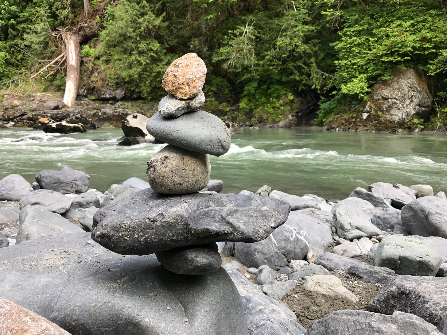 A wider shot of the small, tumbled stone cairn next to the Stillaguamish River.