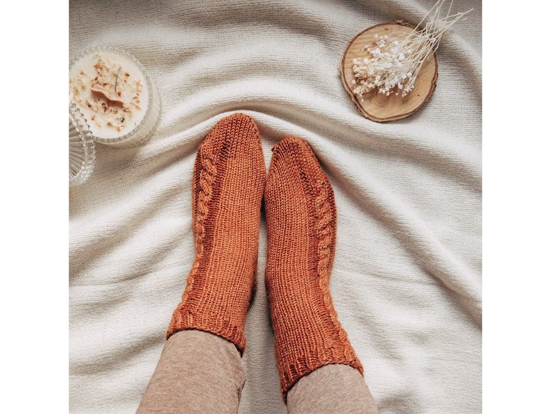 May include: A pair of knitted socks in a rust orange color with a cable knit pattern.