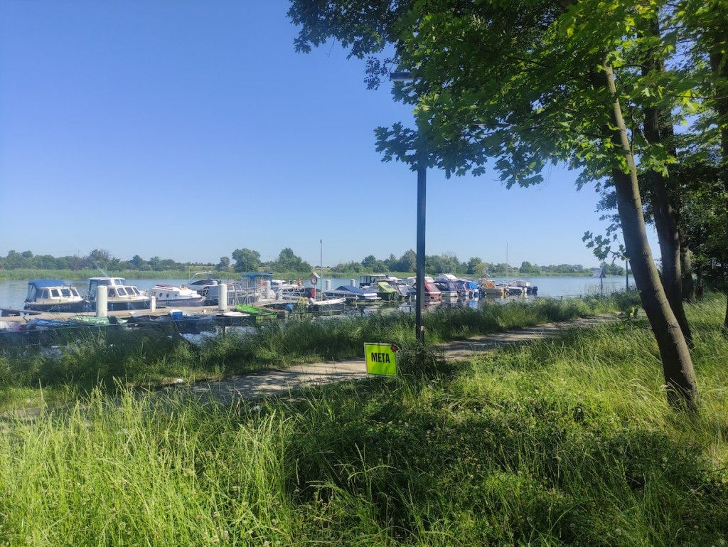 Finish ("meta") sign on the path after the event, with small boats in the marina behind