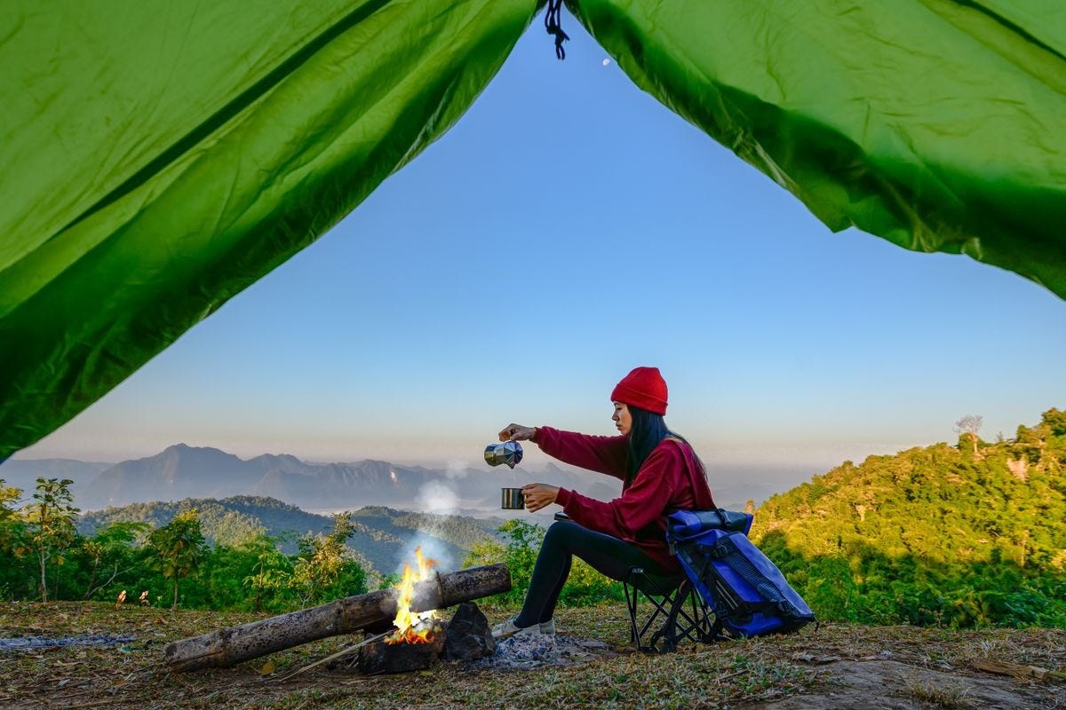 View from inside green tent of woman enjoying hot drink in front of campfire View from inside green tent of woman enjoying hot drink in front of campfire