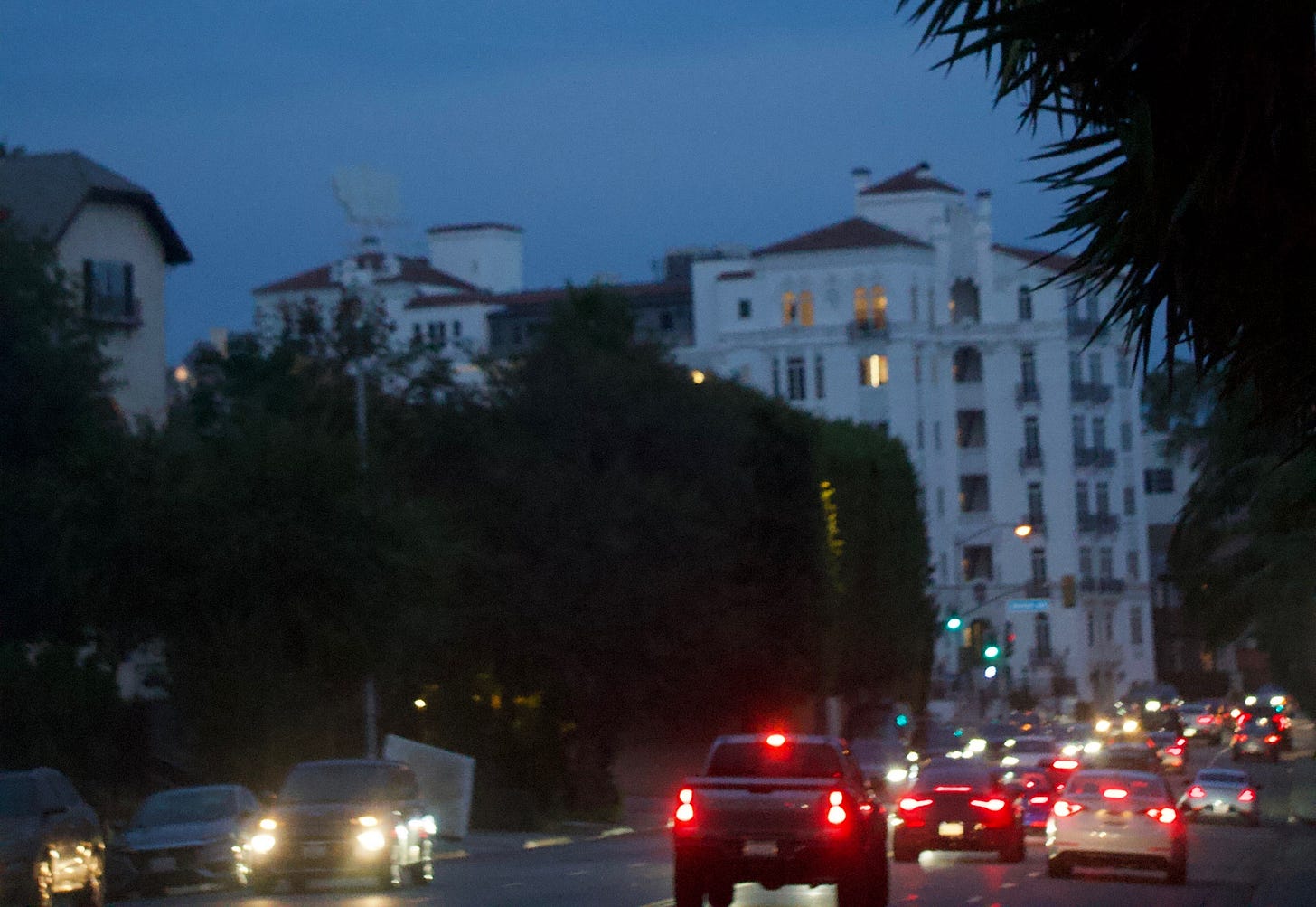 Evening street scene with traffic moving toward a large white building in the distance, headlights glowing as cars drive through the city at dusk. Evening street scene with traffic moving toward a large white building in the distance, headlights glowing as cars drive through the city at dusk.