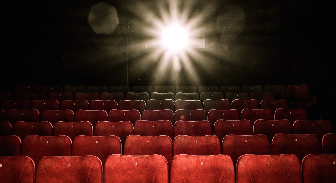 A dark cinema with red velvet seats with gold numbers on and a light shining behind them
