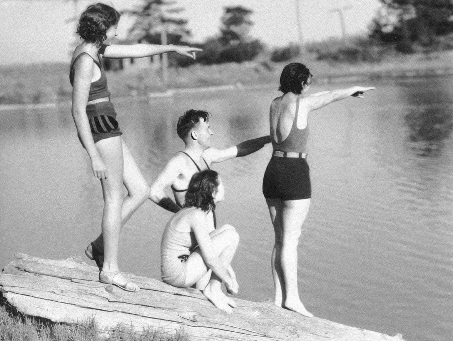 Three girls and one boy hang out in their swimwear at the edge of lake.