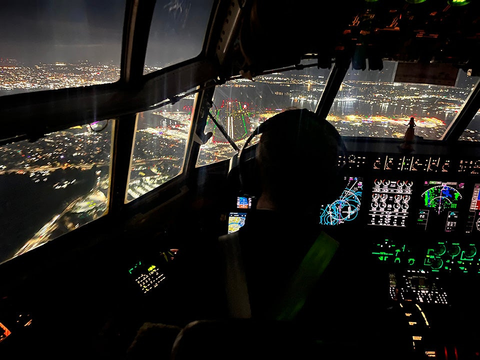 Pilot looking out over New York, the lights of the city shining bright, as he flies at nightt. 