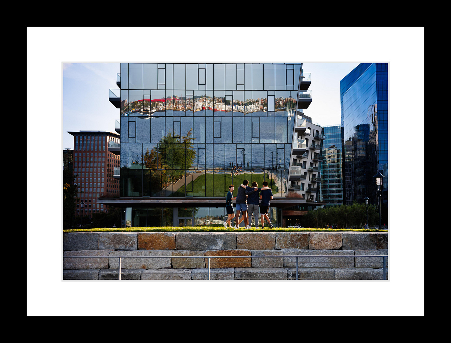 Golden reflections of boats and buildings layered across Boston Harbor at dusk.