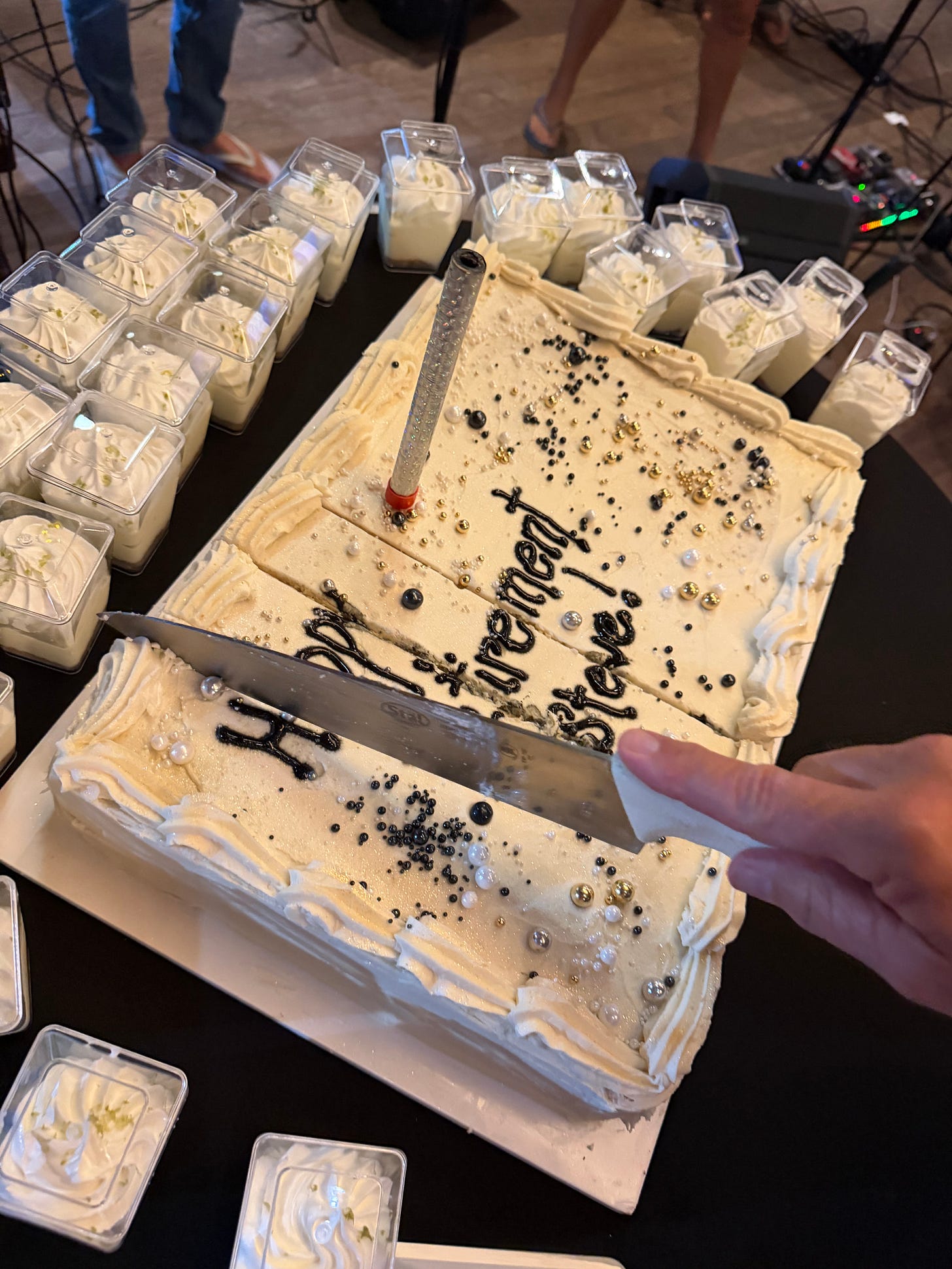 white cake with white frosting and black writing, being cut with a white handled knife