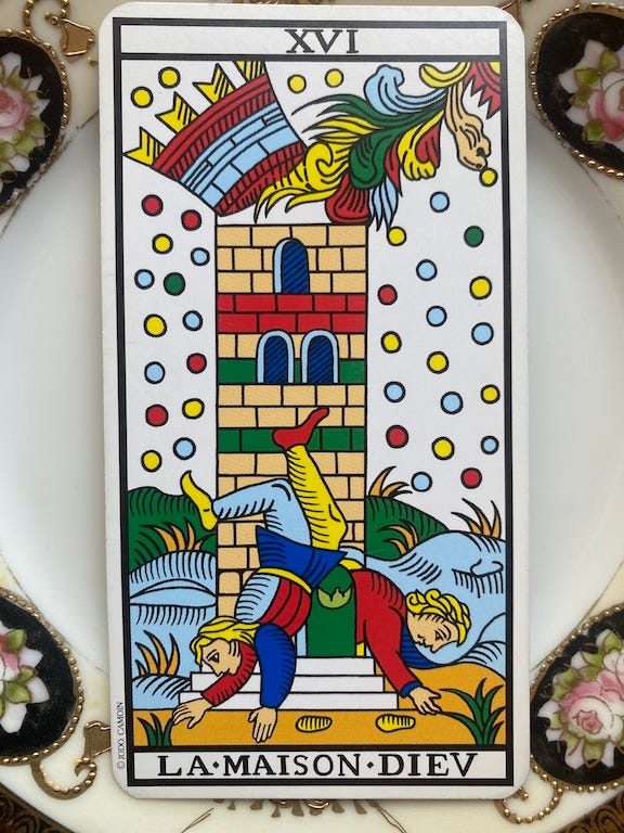 A tarot card lying on a plate, which is only partly shown. The card shows a tower whose turret is splitting off from the main body of the tower, and from which a creature, possibly a Dragon, colored pale blue, golden, flesh, deep red and dark green, is emerging. Dots of the same colour as the creature fall all around the tower. The landscape the tower is sitting in has a dark green background, a pale blue set of closer tile with dark gold colored plants growing out of them, and the steps of the tower which are white, are standing in a dark gold foreground with dark green spiky plants growing out of them. Tow figures, who could be falling, or rising, or dancing are at the bottom of the tower, dressed in bright red, deep blue, and pale blue. In the top of the card are the roman numerals XV1 for 16 and in the bottom are the words La Maison Diev.