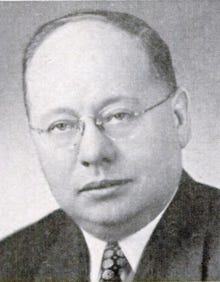 A person wearing glasses and a suit

Description automatically generated