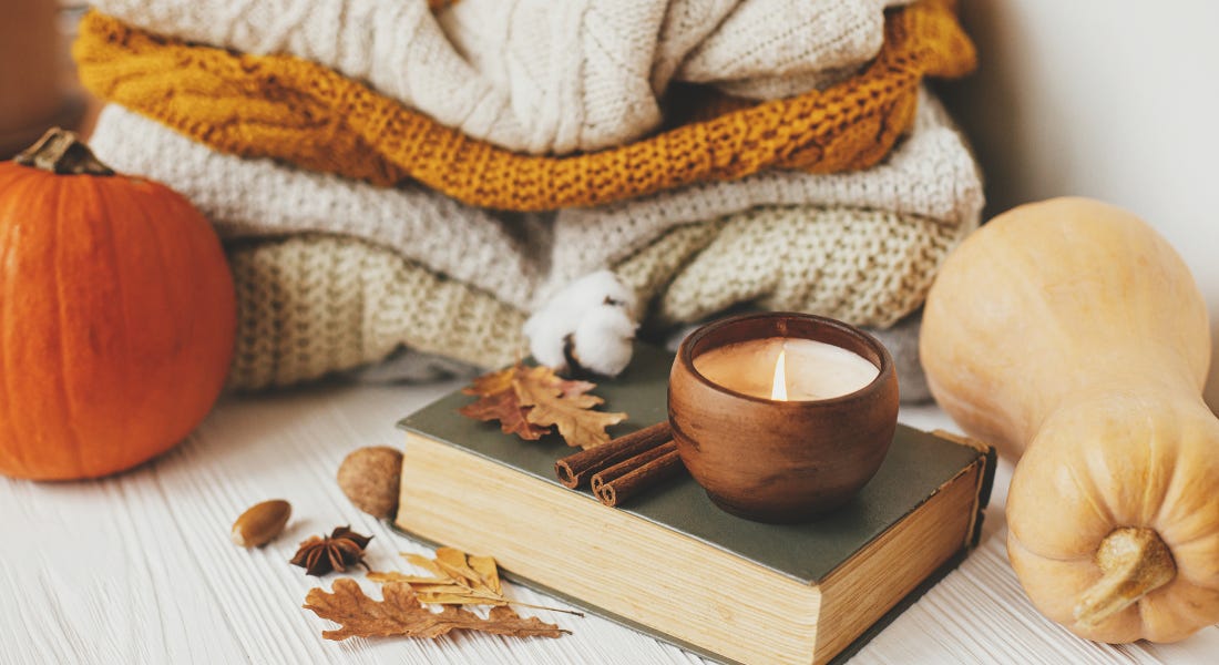 A vignette with pumpkins, a pile of blankets, and a book with leaves on top A vignette with pumpkins, a pile of blankets, and a book with leaves on top
