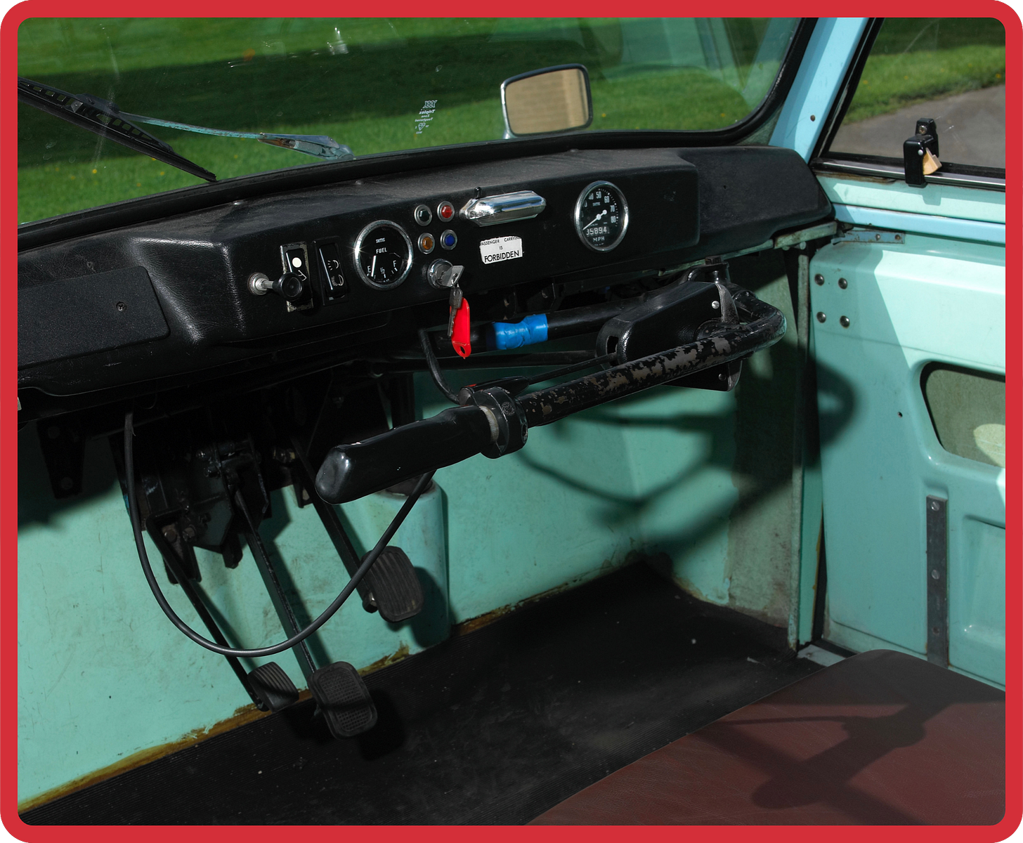 A photo of the inside of an invalid carriage shows the dashboard, front windscreen and a corner of the brown leather seat. The fibreglass frame is a vibrant teal-blue, and instead of a steering wheel there is a left-handed steering bar, and a sign which reads “Passenger Carrying is Forbidden”. A photo of the inside of an invalid carriage shows the dashboard, front windscreen and a corner of the brown leather seat. The fibreglass frame is a vibrant teal-blue, and instead of a steering wheel there is a left-handed steering bar, and a sign which reads “Passenger Carrying is Forbidden”.