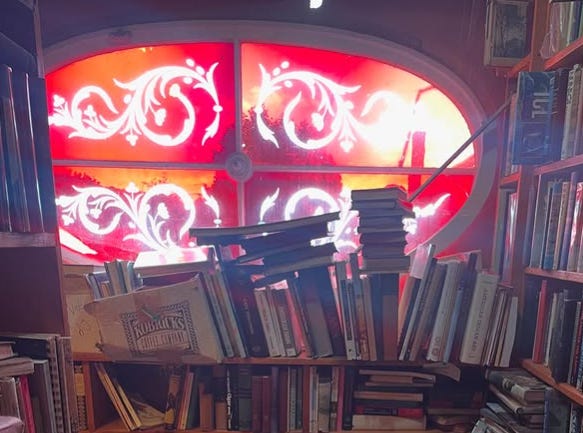A red stained glass window in a bookstore that has books overflowing from the shelves A red stained glass window in a bookstore that has books overflowing from the shelves