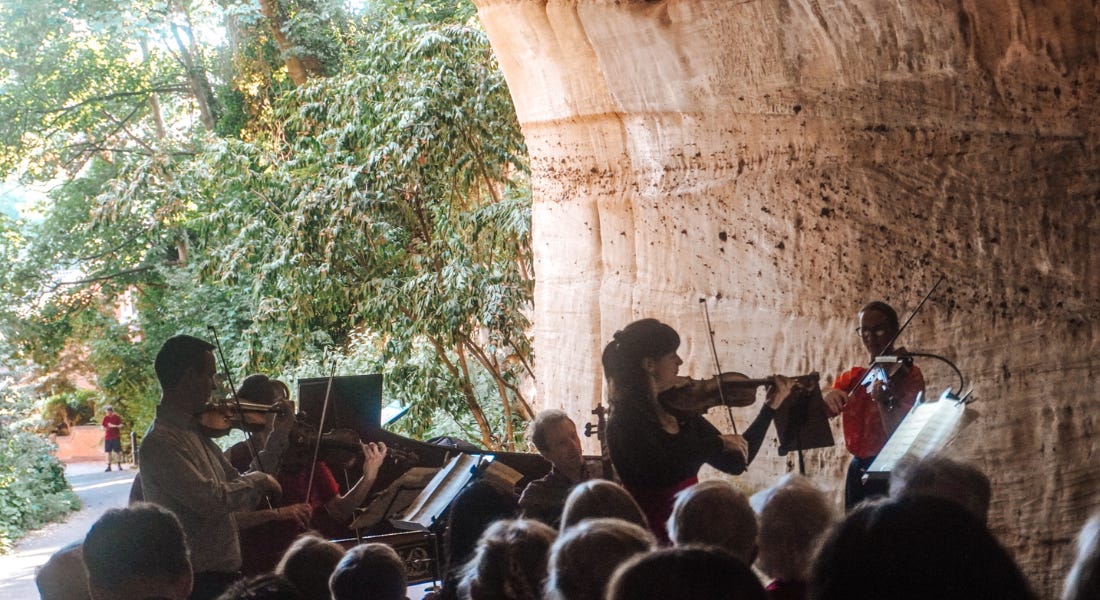 A group of string musicians playing in a cave tunnel, with an audience in front of them A group of string musicians playing in a cave tunnel, with an audience in front of them