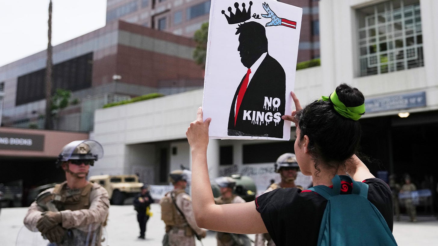 A demonstrator holds a sign in front of U.S. Marines during a protest Saturday, June 14, 2025, in Los Angeles.