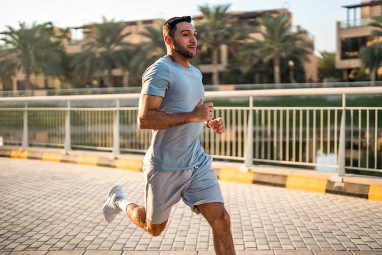 A man running outdoors on a paved pathway surrounded by palm trees and buildings.