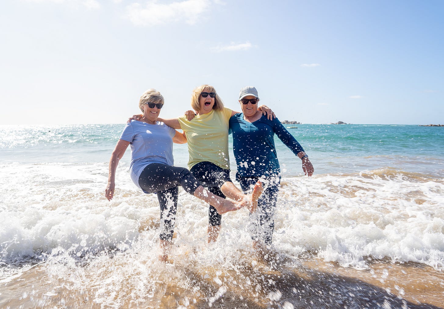 three older women kicking water in the surf having a great time
