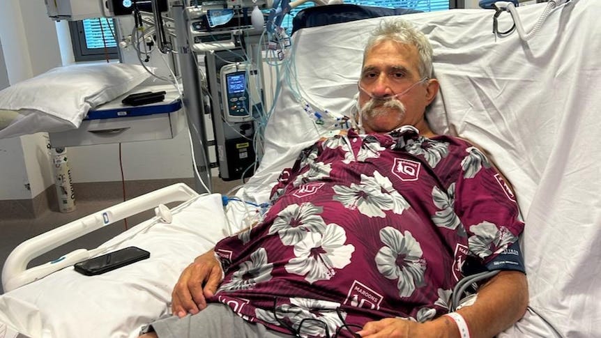 A man wearing a maroon shirt on a hospital bed. A man wearing a maroon shirt on a hospital bed.