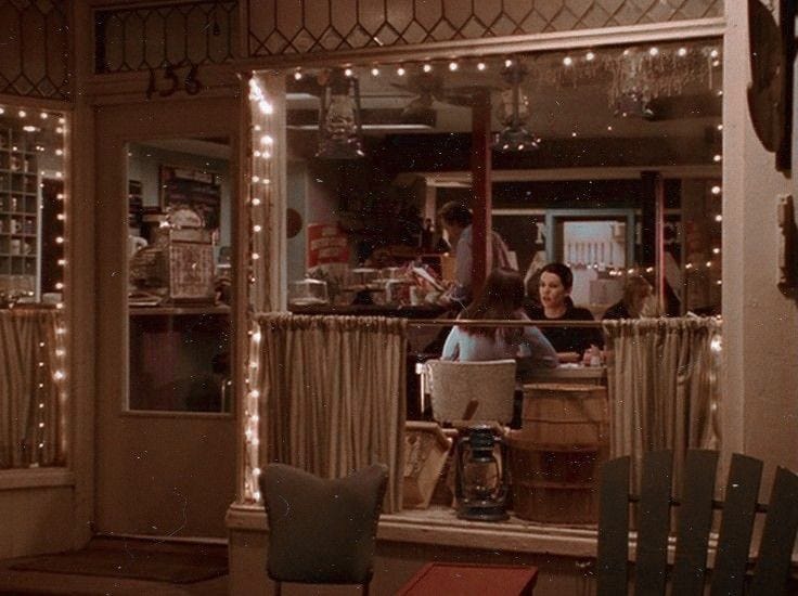 This may contain: two people sitting at a table in front of a window with christmas lights on it