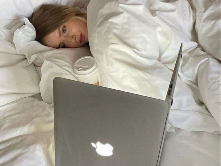 This may contain: a woman laying in bed with an apple laptop