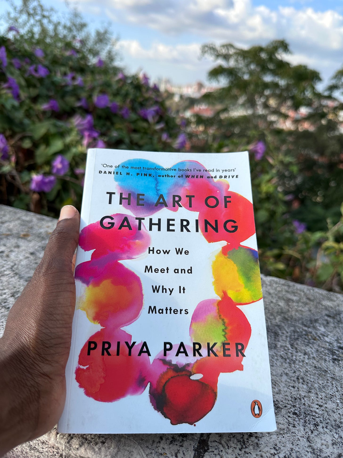The Art of Gathering by Priya Parker, held outdoors near purple flowering shrubs