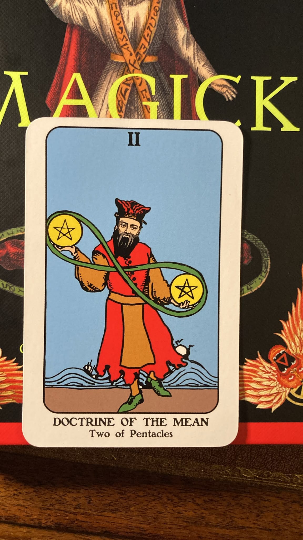 The Two of Pentacles card from The Philosopher’s Tarot, titled Doctrine of the Mean, showing a red-robed philosopher juggling two golden pentacles connected by a green infinity symbol. The Two of Pentacles card from The Philosopher’s Tarot, titled Doctrine of the Mean, showing a red-robed philosopher juggling two golden pentacles connected by a green infinity symbol.