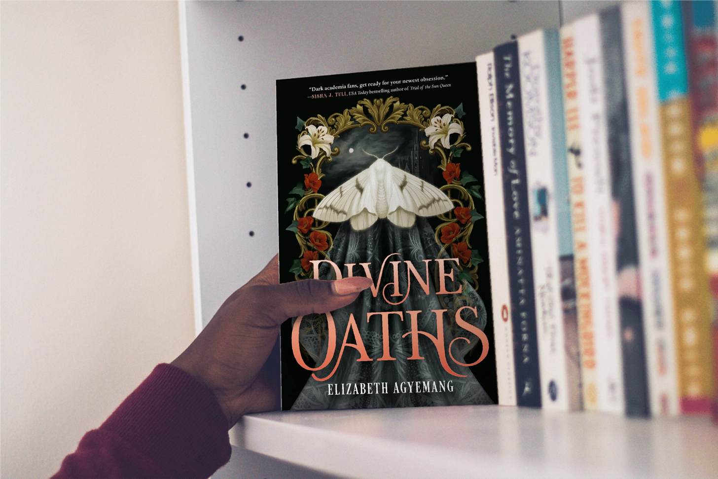 Book "Divine Oaths" by Elizabeth Agyemang being pulled of a bookshelf with other books Book "Divine Oaths" by Elizabeth Agyemang being pulled of a bookshelf with other books