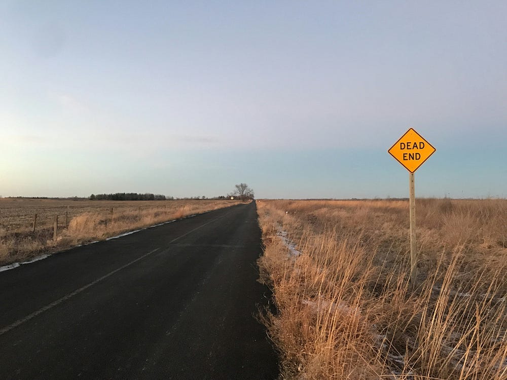 gravel road going straight to the distance with a yellow dead end sign to the right.