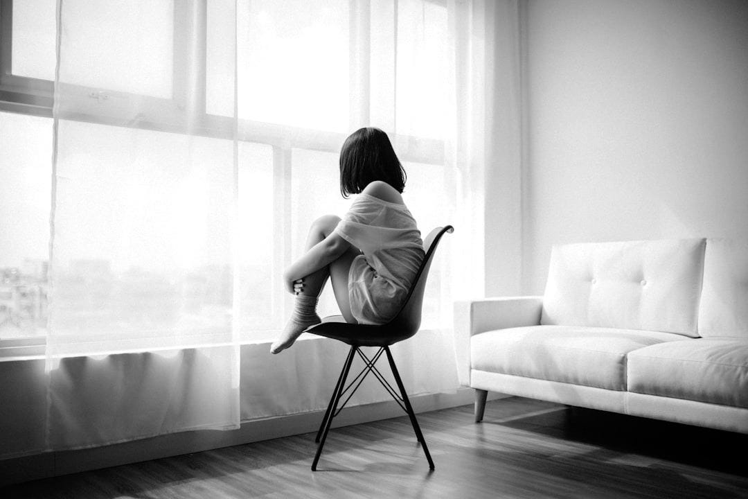woman sitting on black chair in front of glass-panel window with white curtains woman sitting on black chair in front of glass-panel window with white curtains