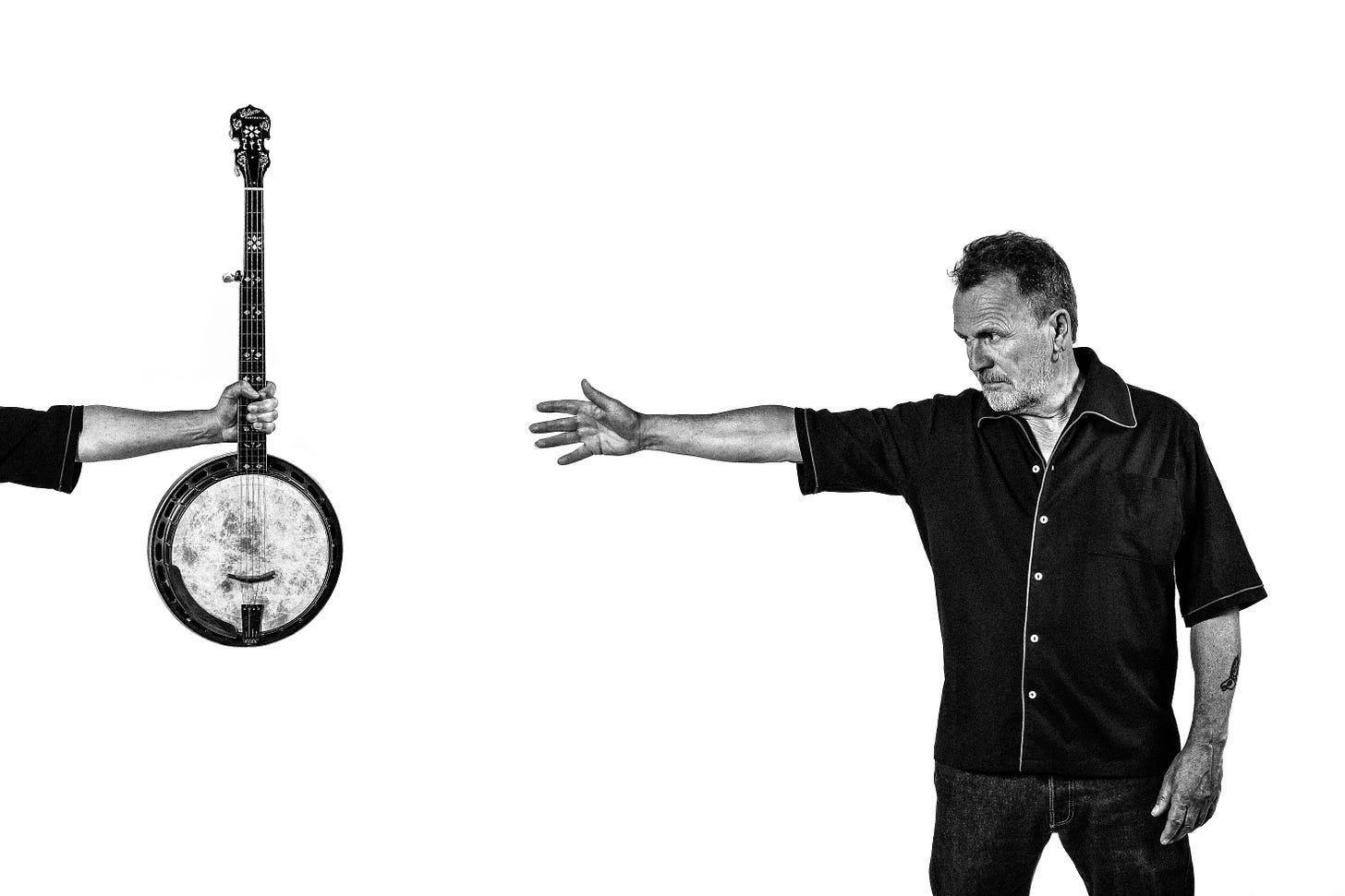 A photo of Martin Simpson, arm outstretched, reaching for a banjo that is held up for him by an arm that definitely, 100% is not just his arm, edited into the photo because they couldn't afford another arm. Like, it definitely isn't wearing the exact same short-sleeved shirt or anything. A photo of Martin Simpson, arm outstretched, reaching for a banjo that is held up for him by an arm that definitely, 100% is not just his arm, edited into the photo because they couldn't afford another arm. Like, it definitely isn't wearing the exact same short-sleeved shirt or anything.