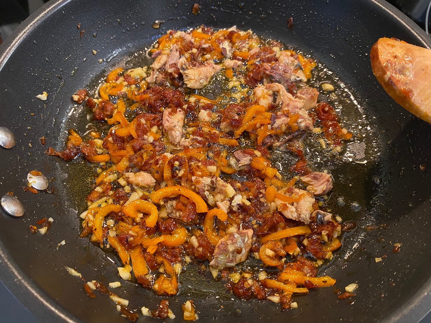 Peppers, sun-dried tomatoes, garlic, and a sardine all frying in oil in a non-stick pan. Peppers, sun-dried tomatoes, garlic, and a sardine all frying in oil in a non-stick pan.