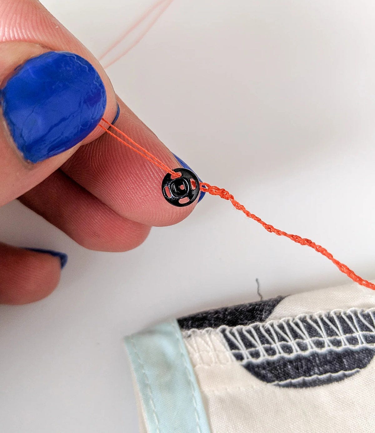 Needle pulling orange thread through fabric near armhole seam with serged edge and light blue binding.