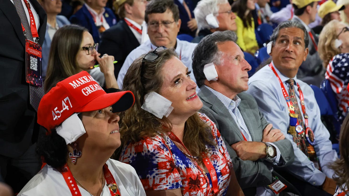 MAGAs dressed in flag paraphenalia stare, rapt, with maxi pads taped to their ears