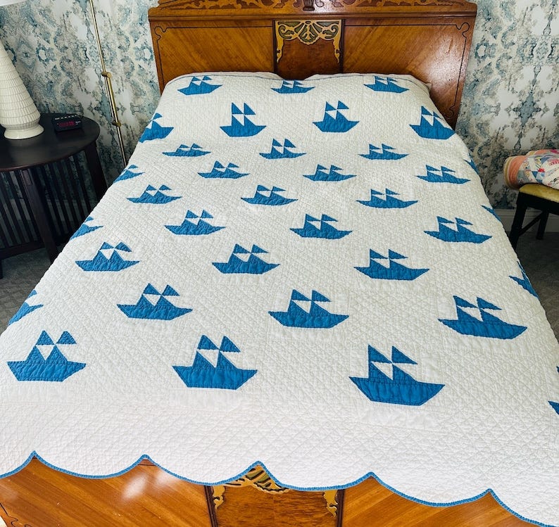 May include: A white quilt with a repeating pattern of blue sailboats. The quilt has a scalloped edge with a blue border. The quilt is on a wooden bed frame. May include: A white quilt with a repeating pattern of blue sailboats. The quilt has a scalloped edge with a blue border. The quilt is on a wooden bed frame.