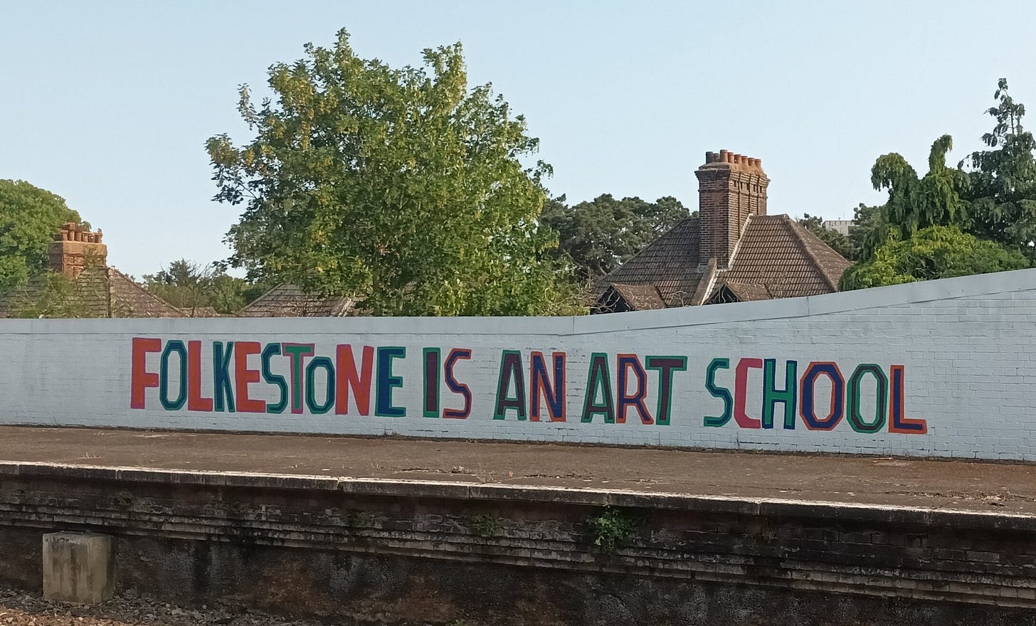 Mural on a wall at Folkestone Train station that reads "Folkestone is an art school" in bold, bright text on a white wall