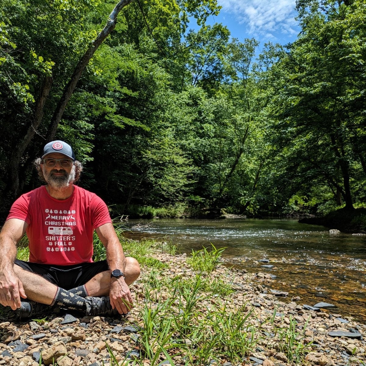 The author sitting crosslegged on a bed of rocks by a shallow creek. The author sitting crosslegged on a bed of rocks by a shallow creek.