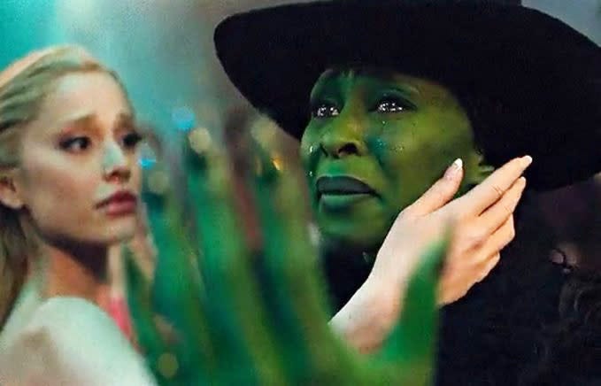 Cena de Wicked. Glinda e Elphaba estão de frente uma pra outra, fazendo um movimento com as mãos. O foco está em Elphaba, que chora olhando pra cima