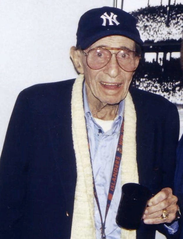 Eddie Layton wearing a New York Yankees cap and holding a mug