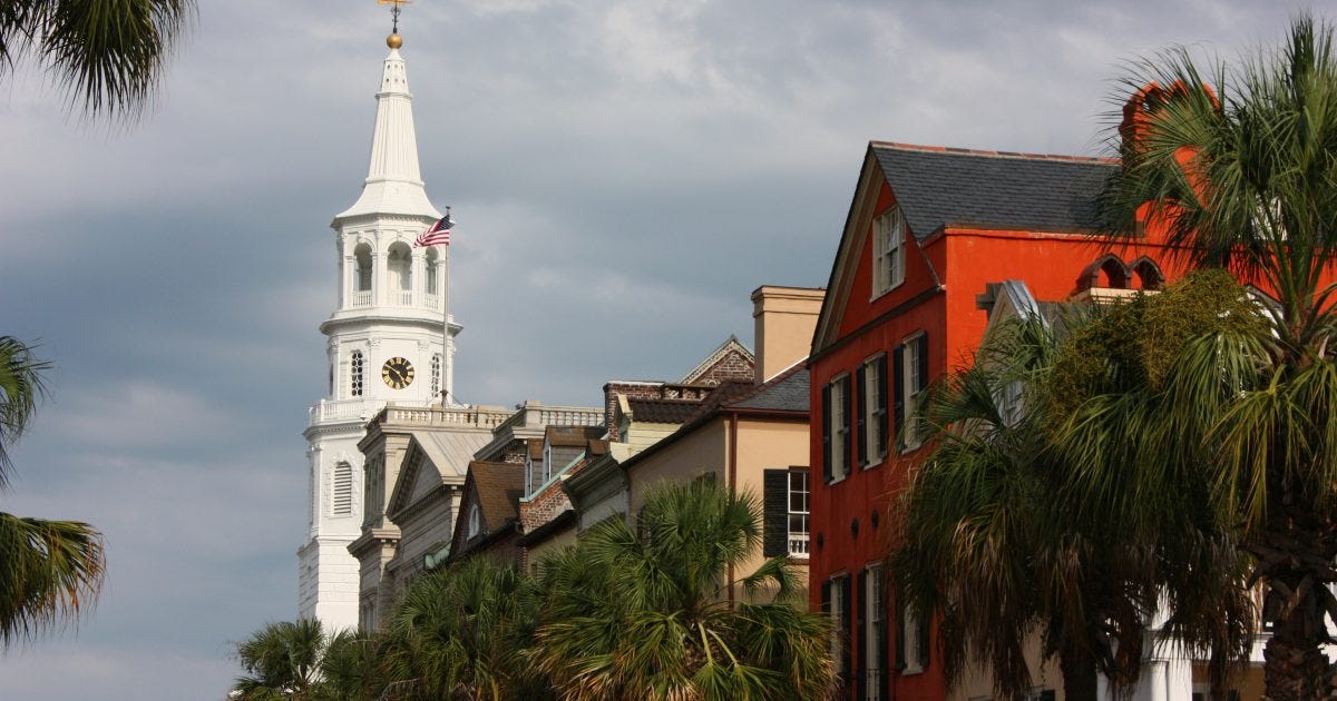 Historic buildings line the waterfront in Charleston, South Carolina, with a prominent white church tower and palm trees under a cloudy sky. Historic buildings line the waterfront in Charleston, South Carolina, with a prominent white church tower and palm trees under a cloudy sky.