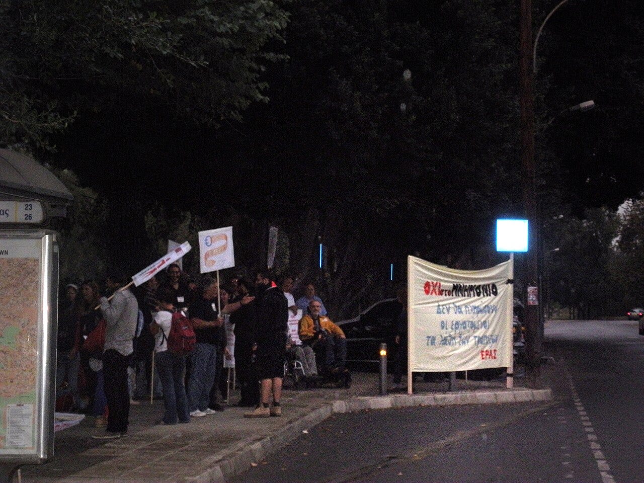 Nighttime street protest with crowd holding signs and banner near bus stop Nighttime street protest with crowd holding signs and banner near bus stop
