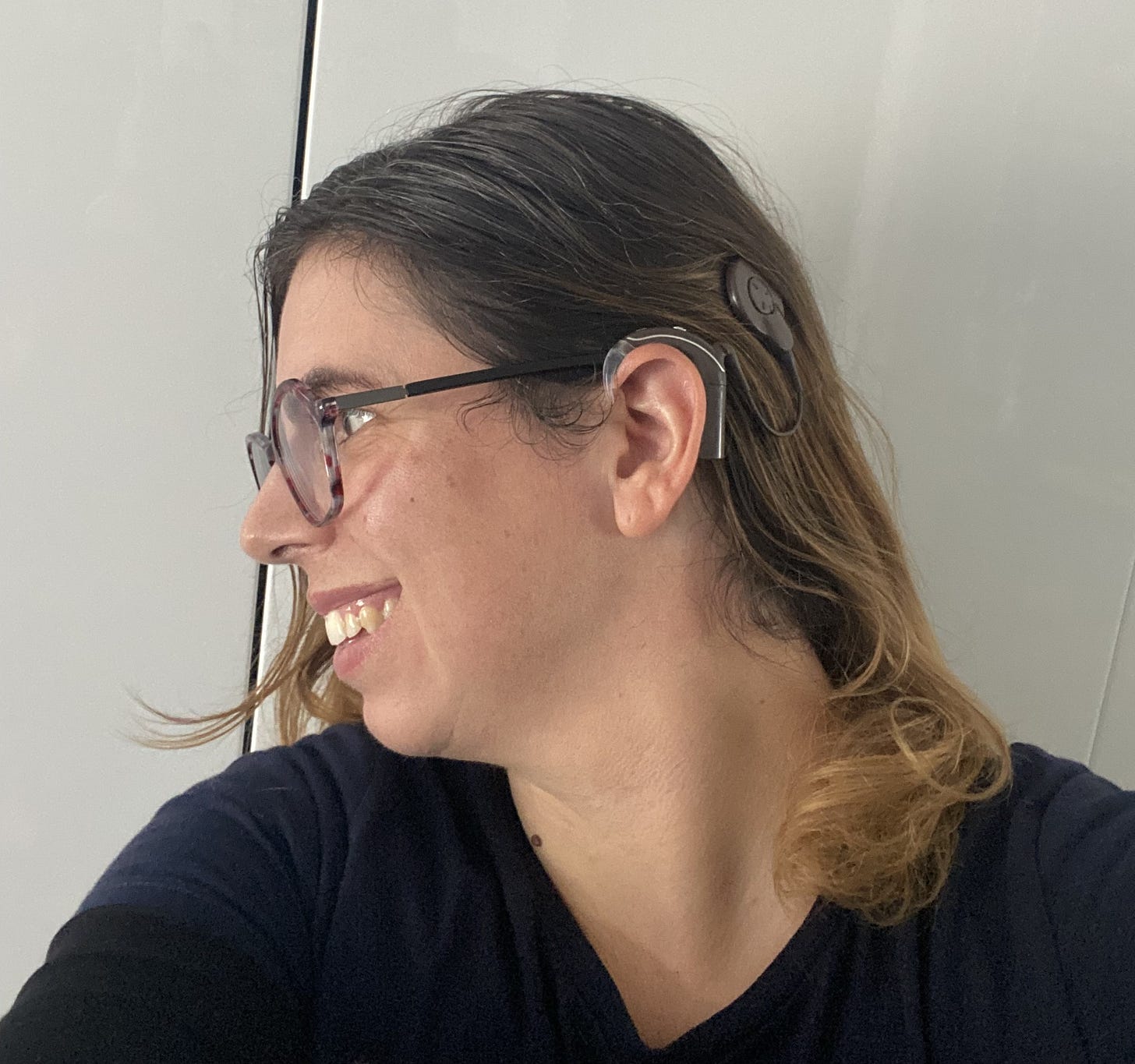 Je suis de profil. Mes cheveux châtains sont longs jusqu’aux épaules. Je suis souriante et j’ai des lunettes. On voit mon implant cochléaire dont le contour est posé sur l’oreille avec un fil qui relie jusqu’à l’antenne collé sur les cheveux un peu en hauteur. Je suis de profil. Mes cheveux châtains sont longs jusqu’aux épaules. Je suis souriante et j’ai des lunettes. On voit mon implant cochléaire dont le contour est posé sur l’oreille avec un fil qui relie jusqu’à l’antenne collé sur les cheveux un peu en hauteur.