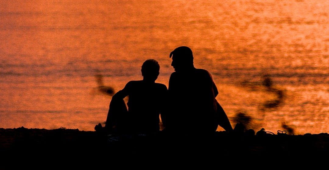 a couple of people sitting on top of a beach a couple of people sitting on top of a beach