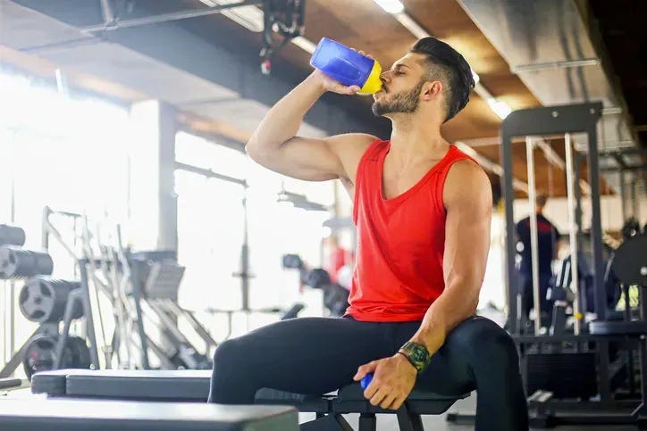 Man in a gym drinking out of a protein shaker bottle.