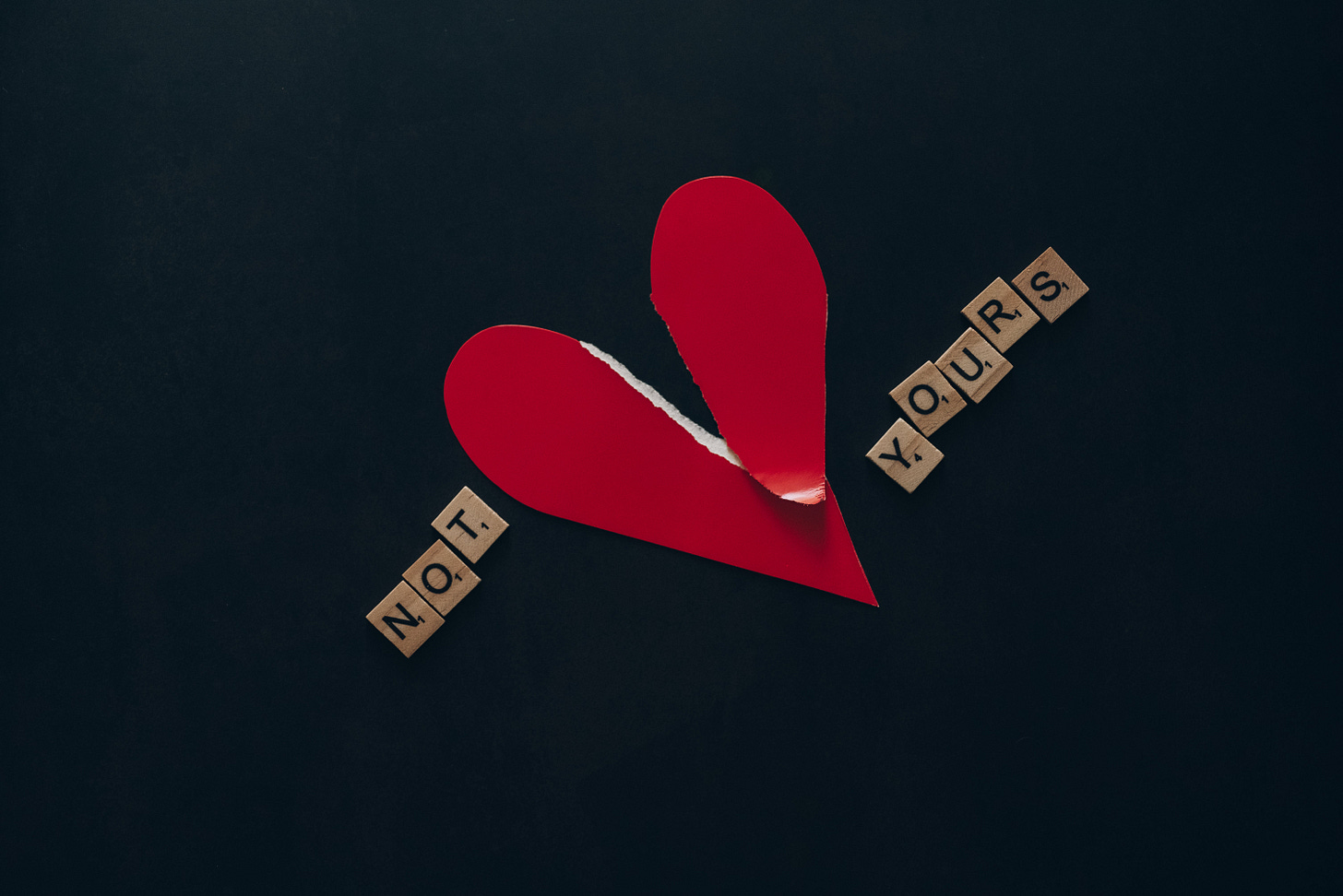 a red paper heart torn in two the words "not" and "yours" on either side a red paper heart torn in two the words "not" and "yours" on either side