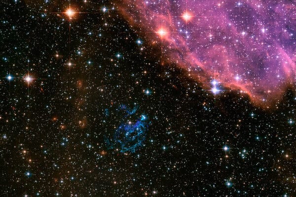 The remnants of a supernova, center bottom in blue-green, near the Small Magellanic Cloud, captured by the Hubble Space Telescope.